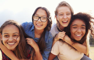 Four teenage girls having fun piggybacking outdoors