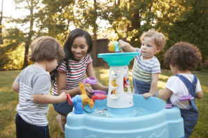 Mother And Young Children Playing With Water Table In Garden